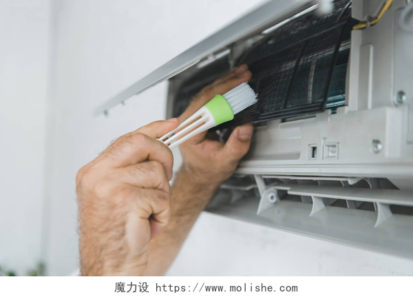 一个拿着刷子的手在清理空调男性工人用刷子清洗空调器的裁剪视图
